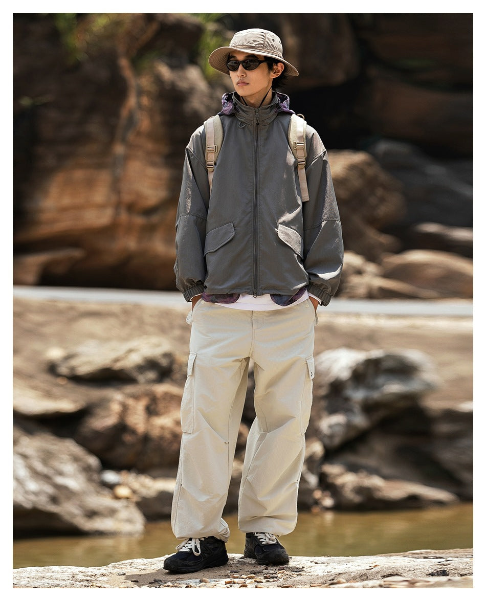 Full-length view of a man wearing a charcoal hooded jacket with flap pockets and light cargo pants.
