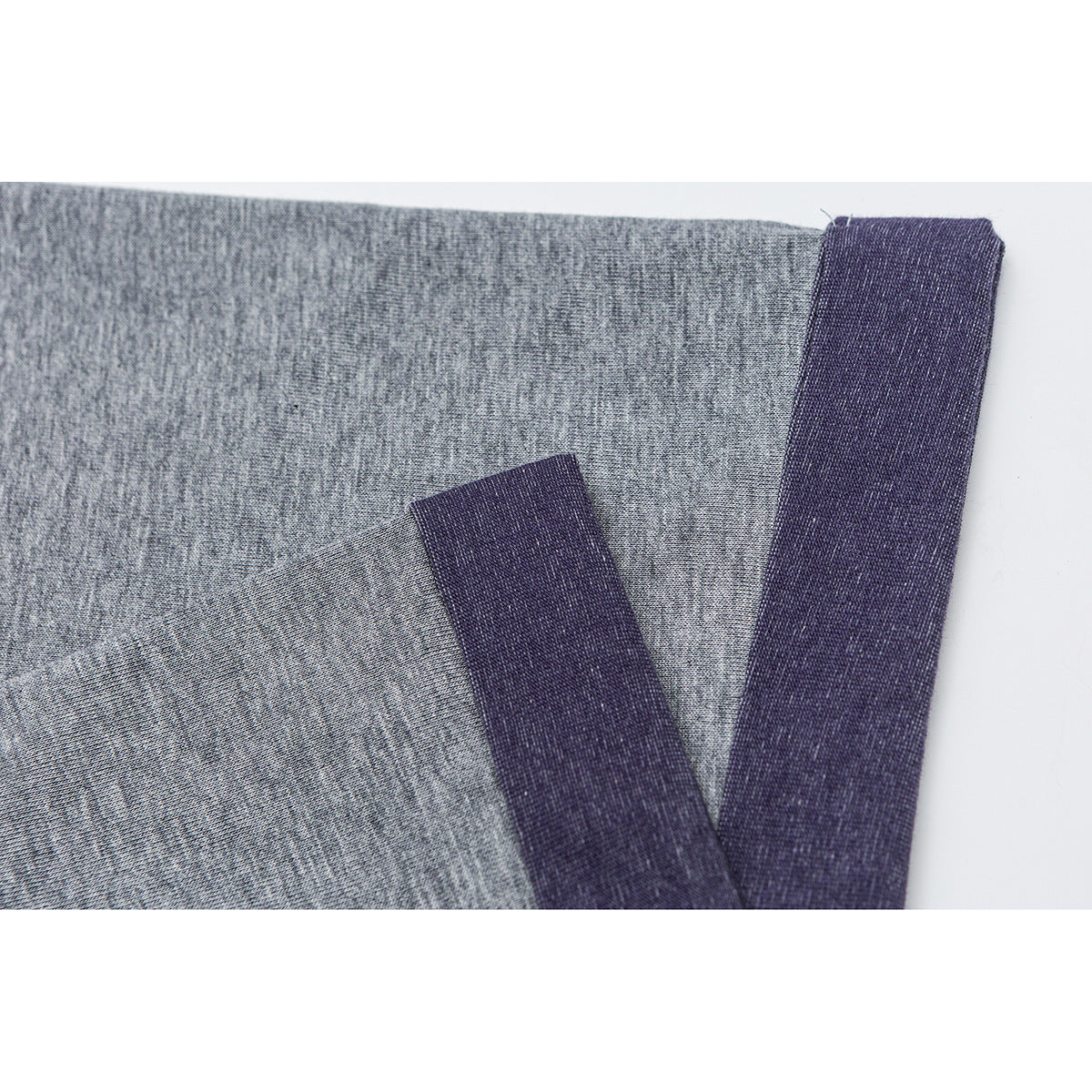 Close-up of heather gray shirt fabric with dark purple trim at the edge and a folded section.
