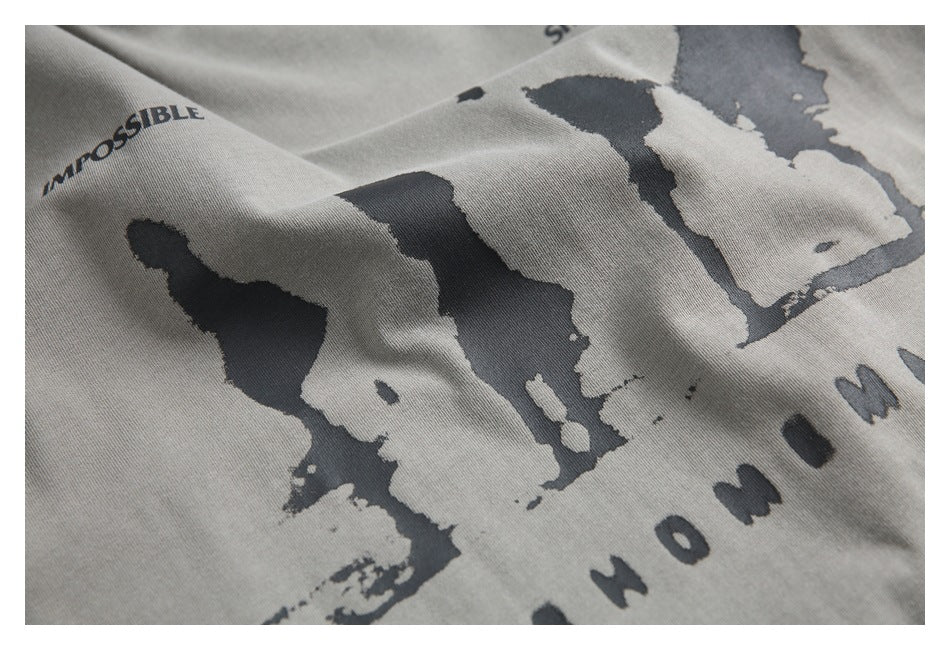 Angled close-up of a gray T-shirt’s dark silhouette graphic and partial English lettering.