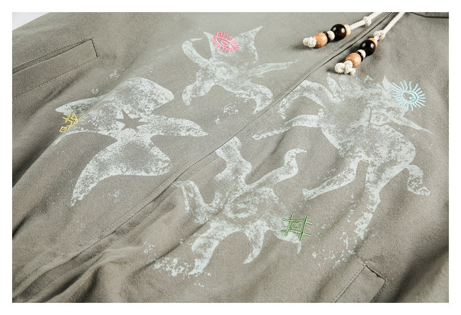 Close-up of a gray-khaki garment with a distressed white animal print and small colored motifs beside a beaded cord.