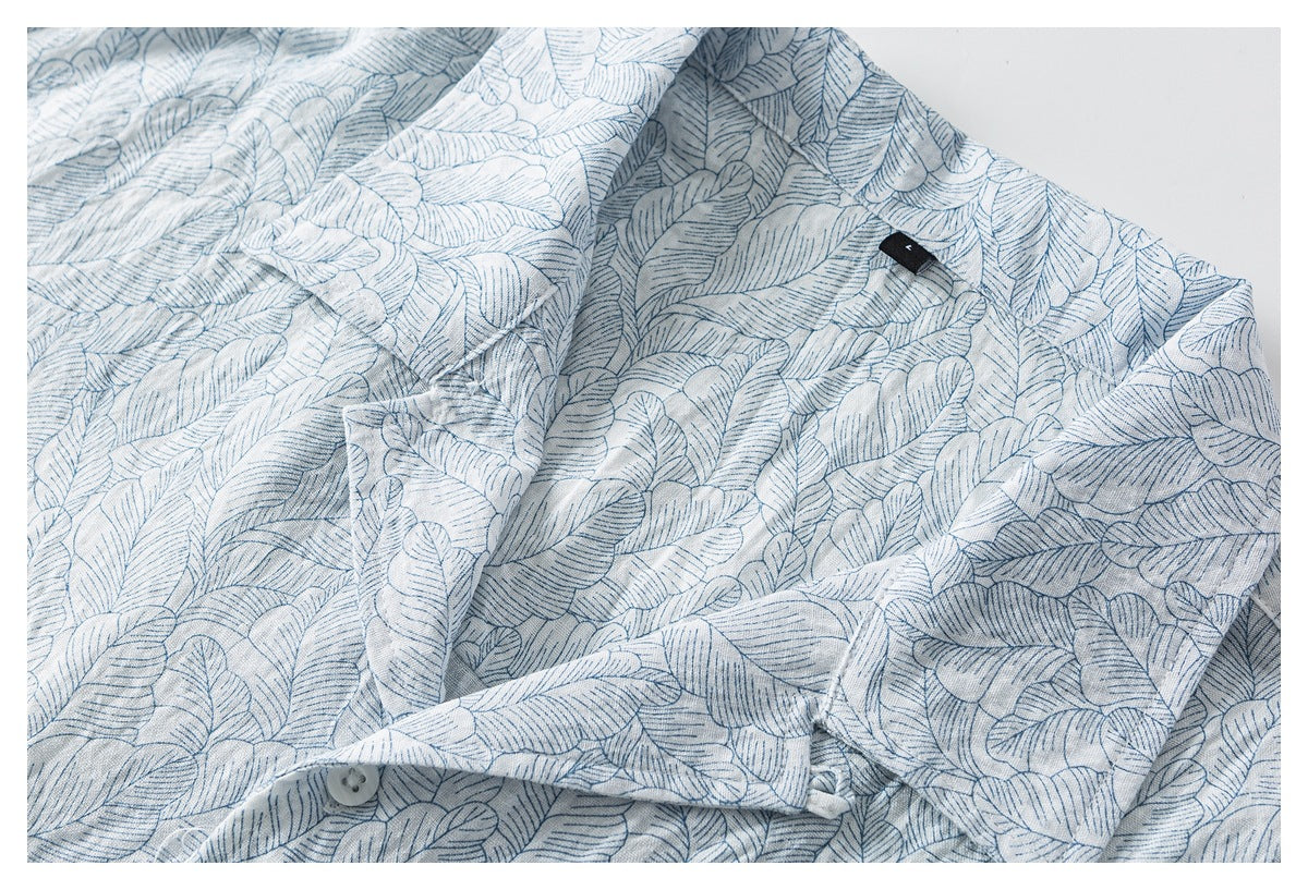Angled close-up of a pale blue leaf-print shirt collar and front placket with a button and small black tag.
