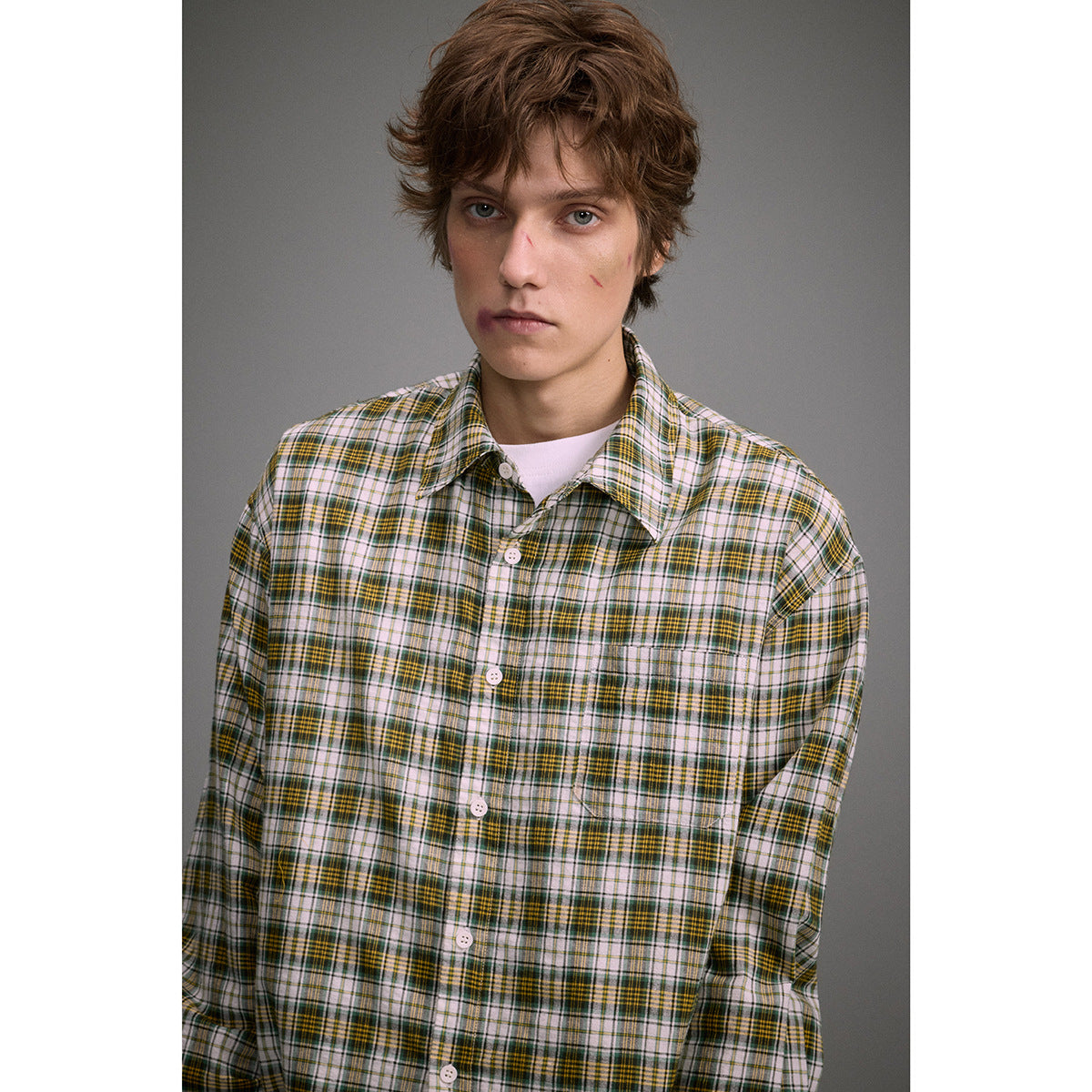Model wearing a white, green, and mustard plaid button-up shirt, shown from the chest up.