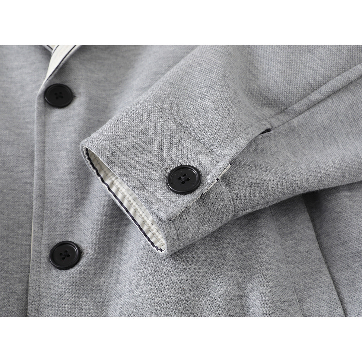 Close-up of a light gray jacket sleeve cuff with a black button and striped lining, beside the front buttons.