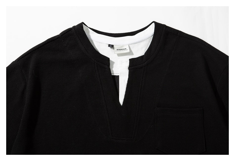 Close-up of a black textured shirt's notched neckline, white inner placket, and chest pocket.