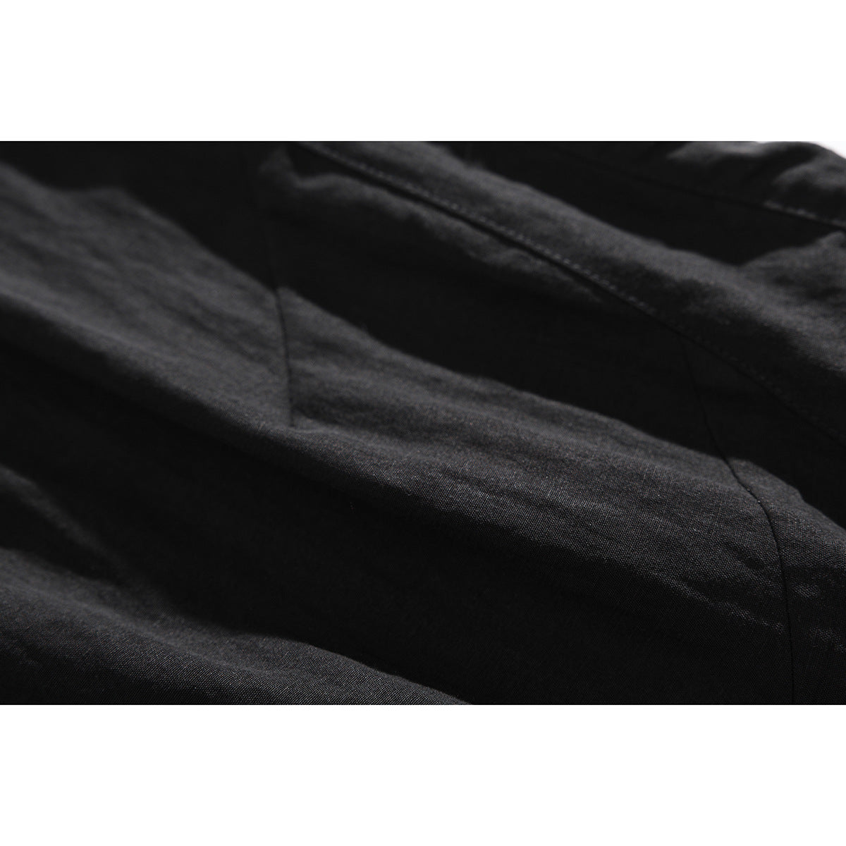 Extreme close-up of black shorts fabric folds and a stitched seam.
