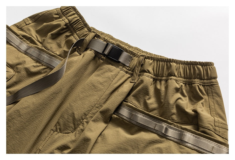 Close-up of olive-brown shorts showing the elastic waistband, belt loops and adjustable webbing strap with buckle.