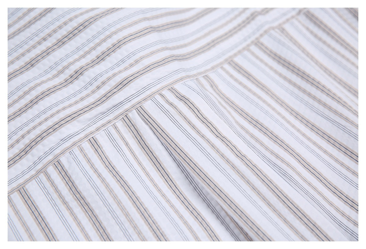 Close-up of white fabric with fine gray and tan stripes and a diagonal stitched seam.