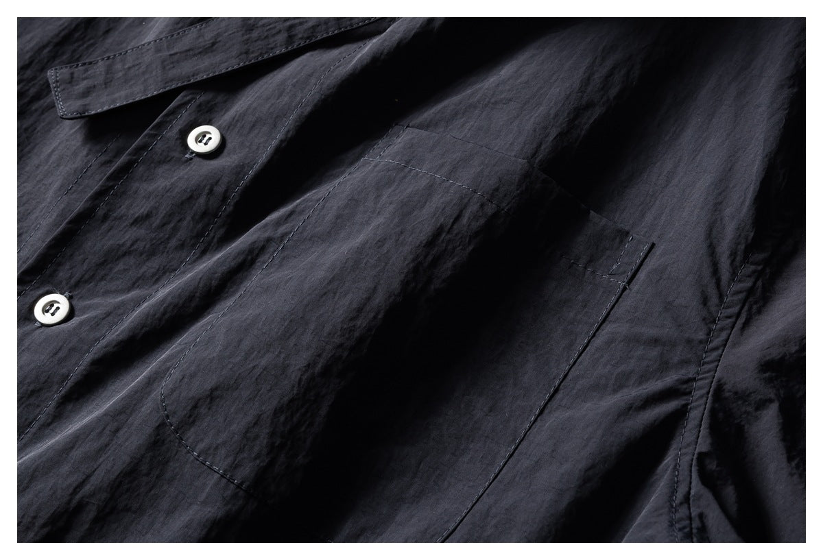 Close-up of the dark shirt's chest pocket, stitching, and two pale buttons.