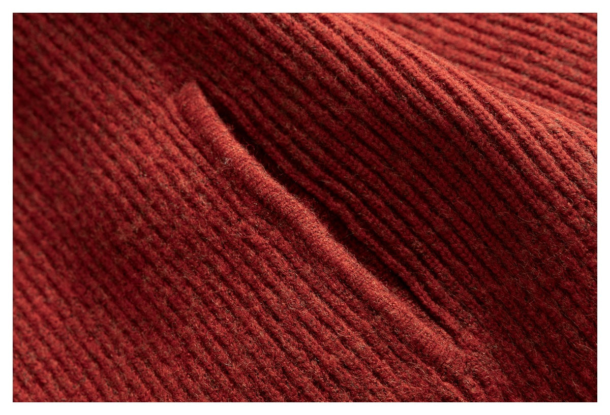 Close-up of the rust-red sweater's rib-knit fabric and raised seam.