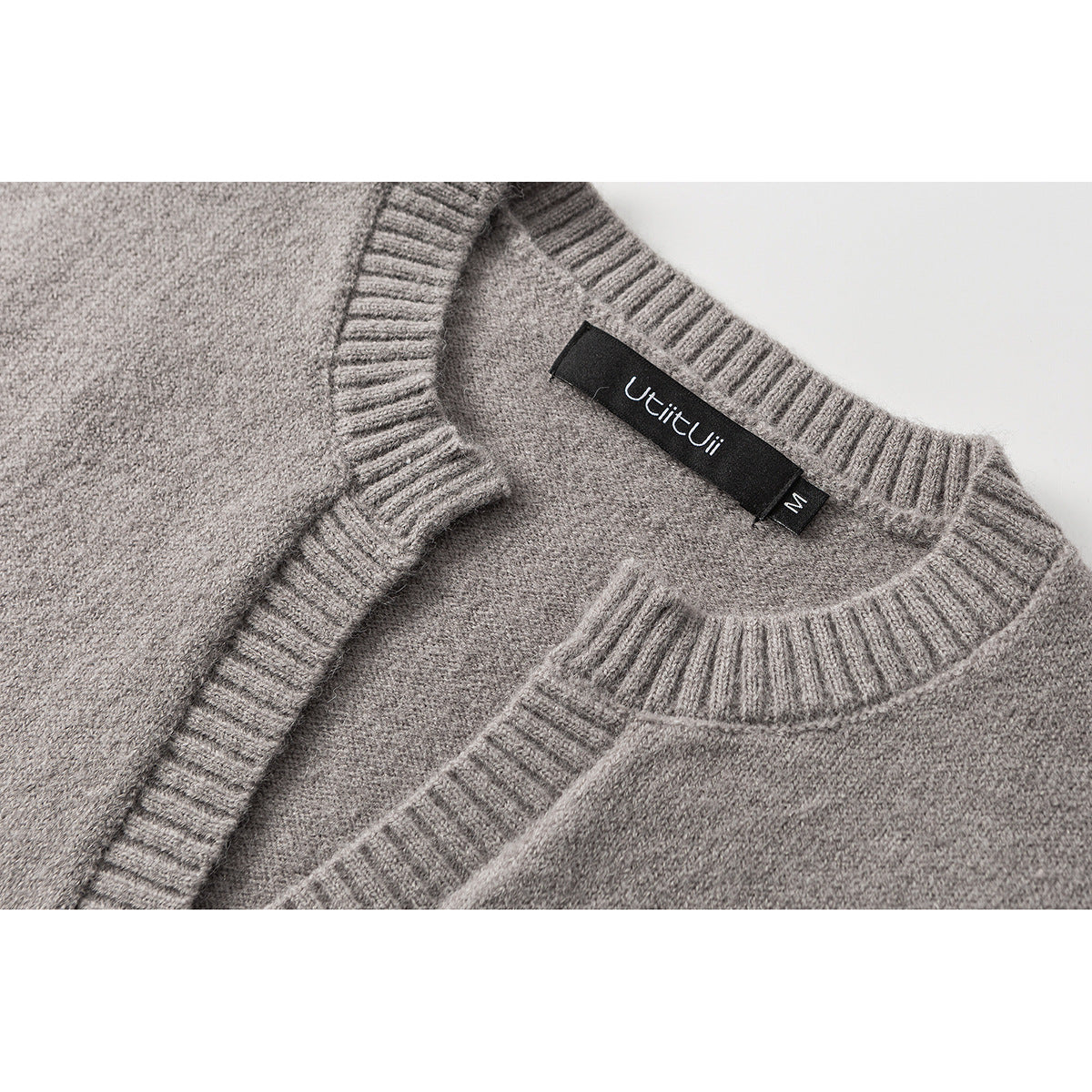Close-up of a gray knit vest neckline with ribbed trim and a black neck label.