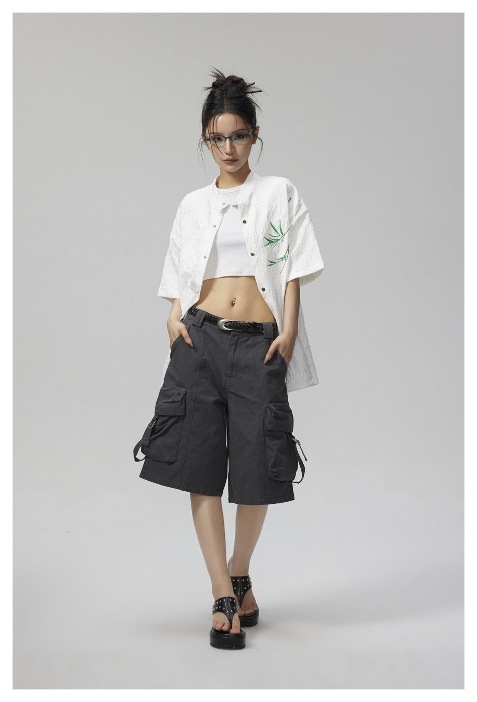 Model wearing the white short-sleeve snap shirt open over a white crop top with gray cargo shorts, front view