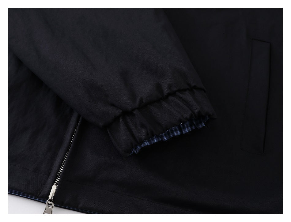 Close-up showing a gathered sleeve cuff, plaid trim, zipper, and pocket on a black garment.