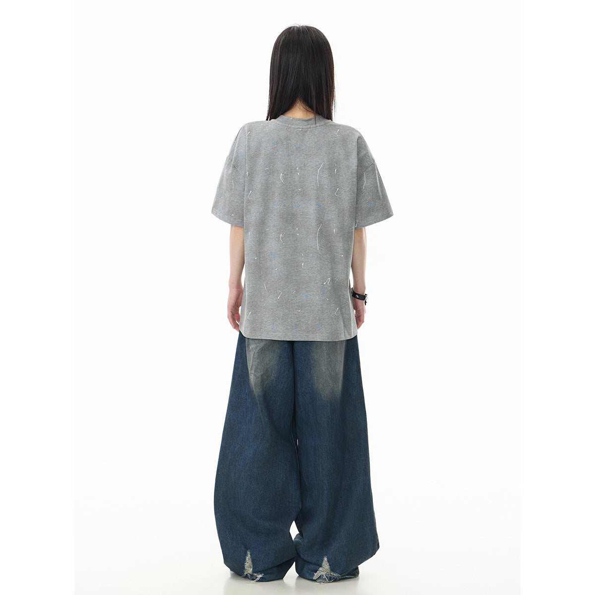 Back view of a model wearing a loose gray short-sleeve T-shirt with scattered flecks and wide dark blue jeans.