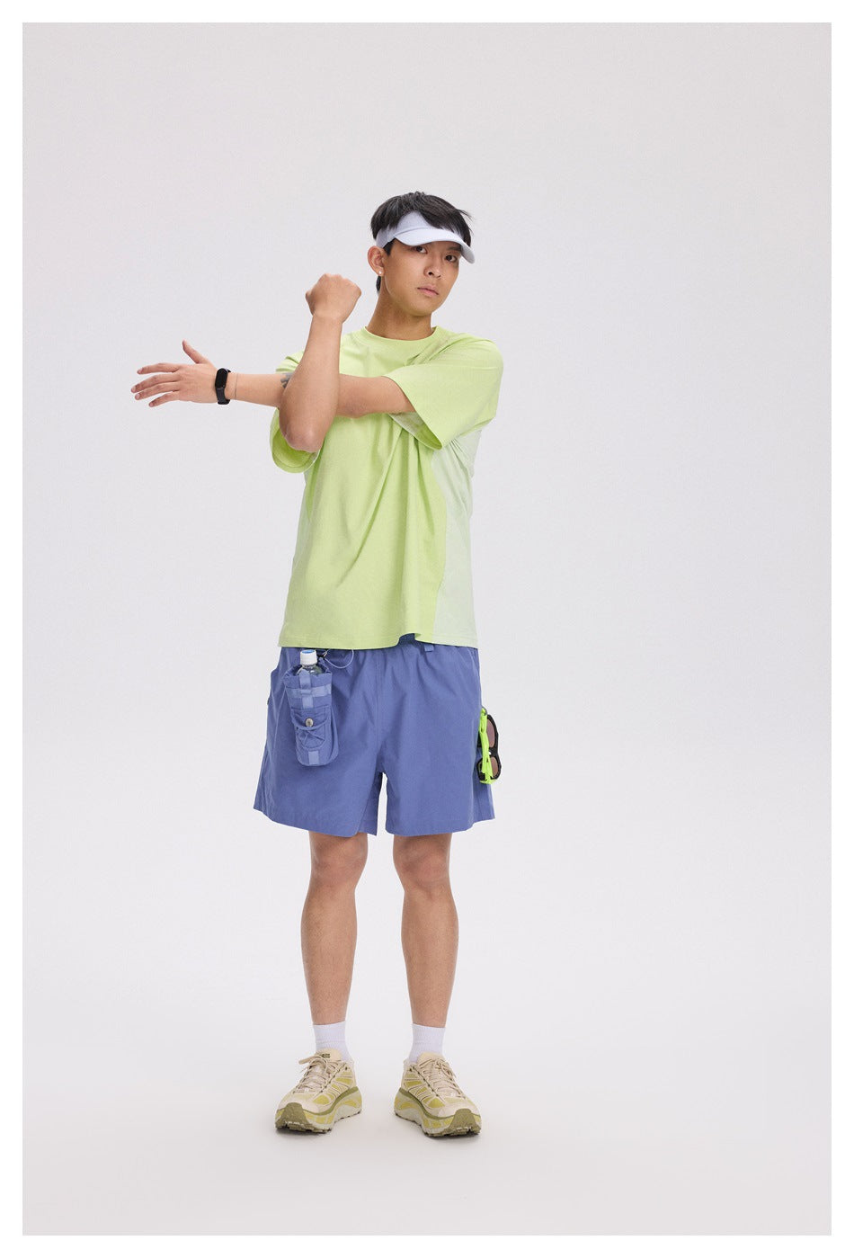 A man models a pale lime short-sleeve T-shirt with blue-violet shorts and a white visor.