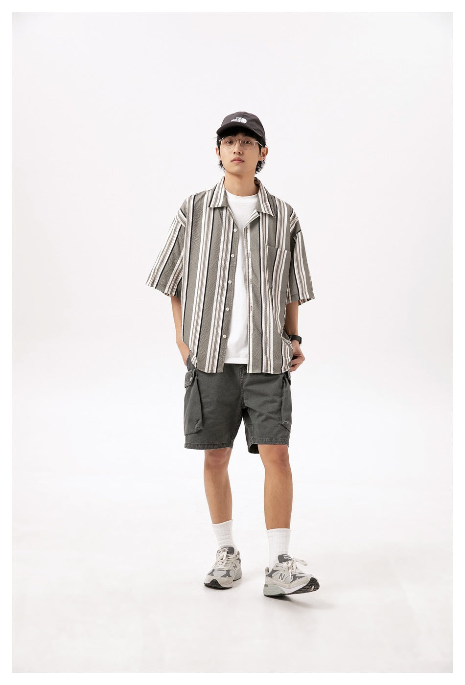 Person wearing washed gray cargo shorts with a striped short-sleeve shirt, white tee, cap and gray sneakers