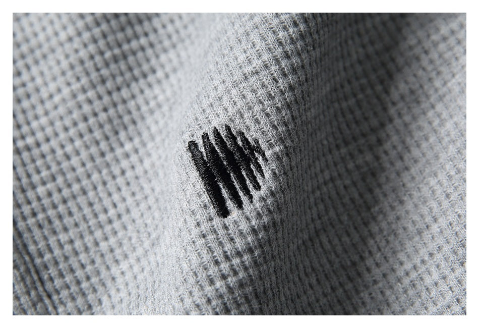 Close-up of a small black embroidered motif on gray textured fabric.