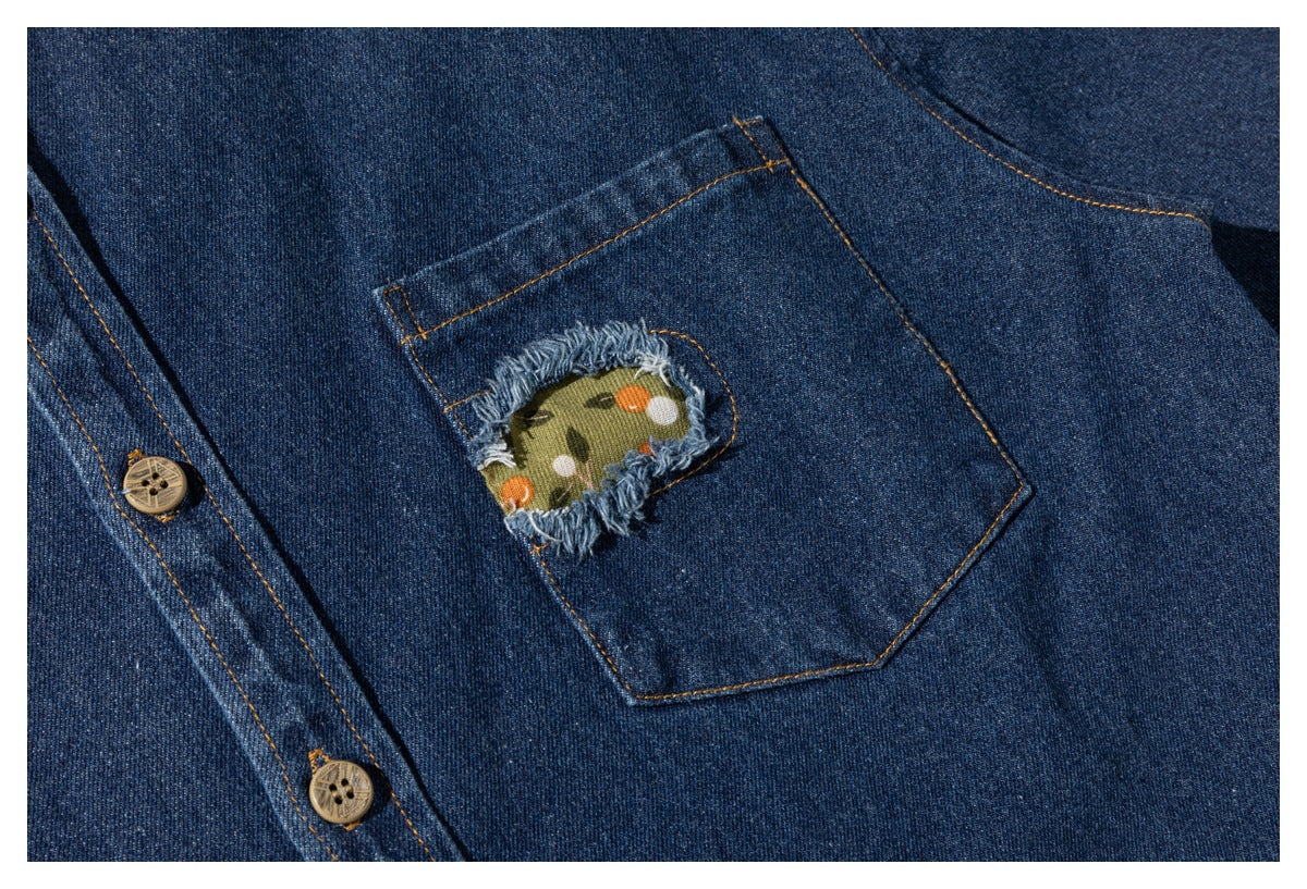 Close-up of a dark blue denim shirt pocket with a frayed opening revealing olive fabric with a small floral print.