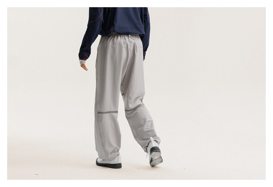 Angled rear view of a cropped model wearing loose light-gray drawstring pants with dark horizontal leg bands.