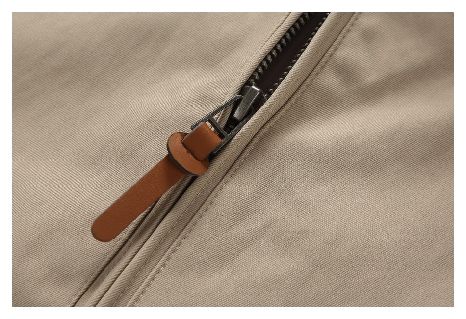 Close-up of a dark zipper with a brown pull tab on beige jacket fabric.