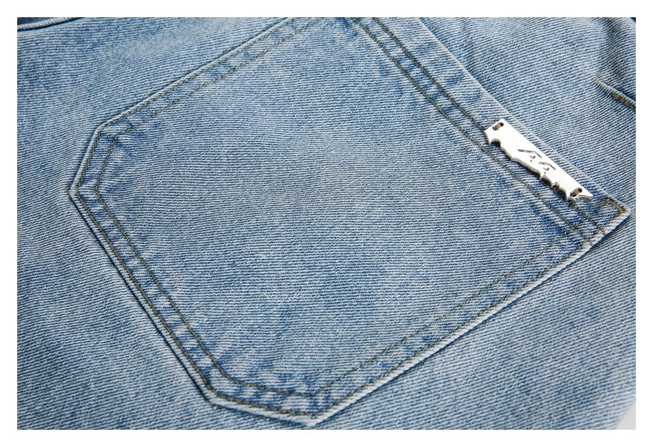 Close-up of a stitched back pocket on light blue jeans with a small metal logo plate.