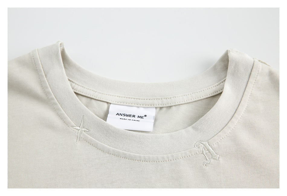 Close-up of an ivory crew neckline, small stitched accents, and a neck label reading “ANSWER ME.”