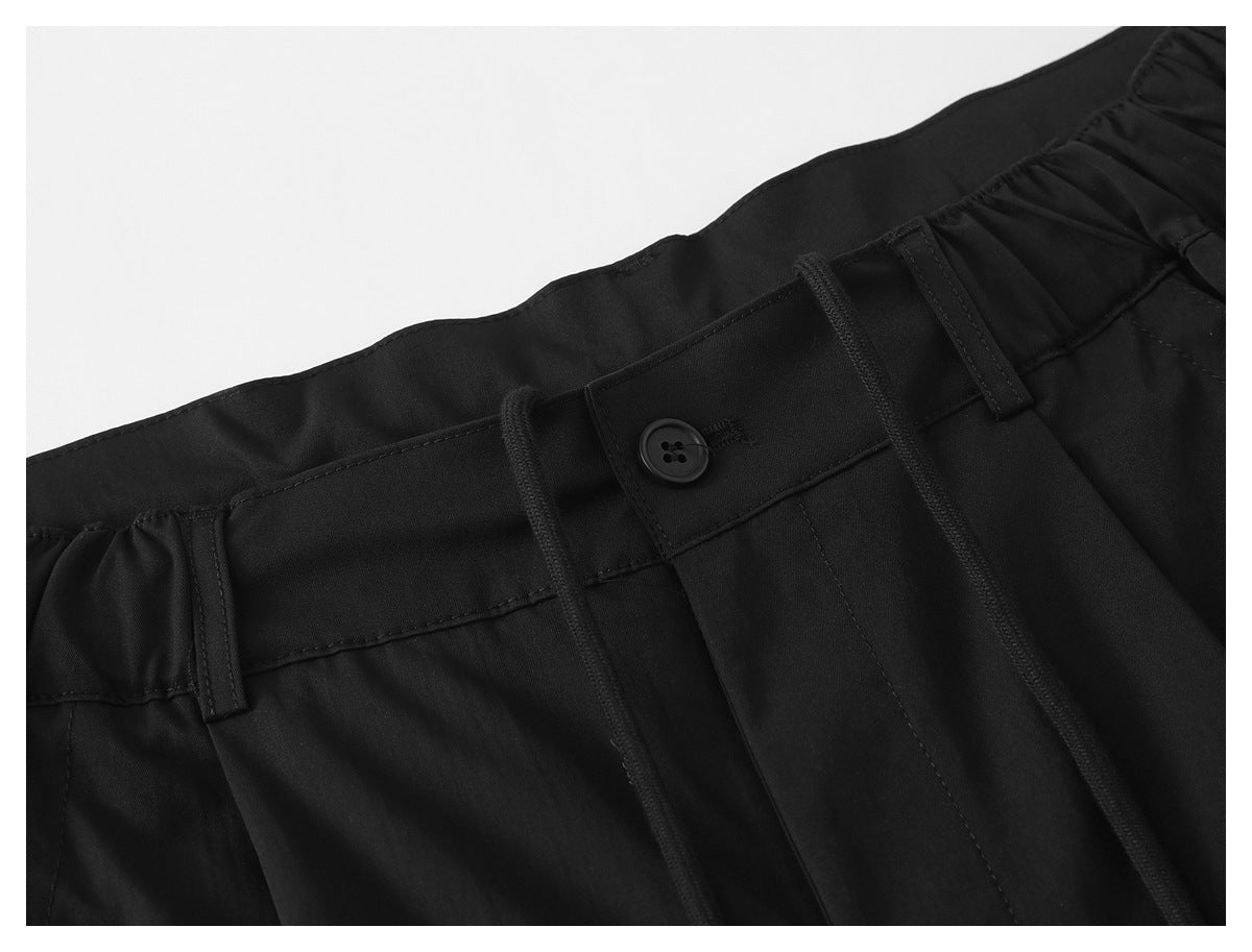 Close-up of black pants showing the button fly, belt loops, and drawstring waistband.