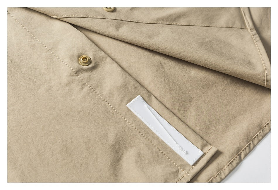 Close-up of the beige shirt's snap fastener, overlapping front placket, and small white inner label.