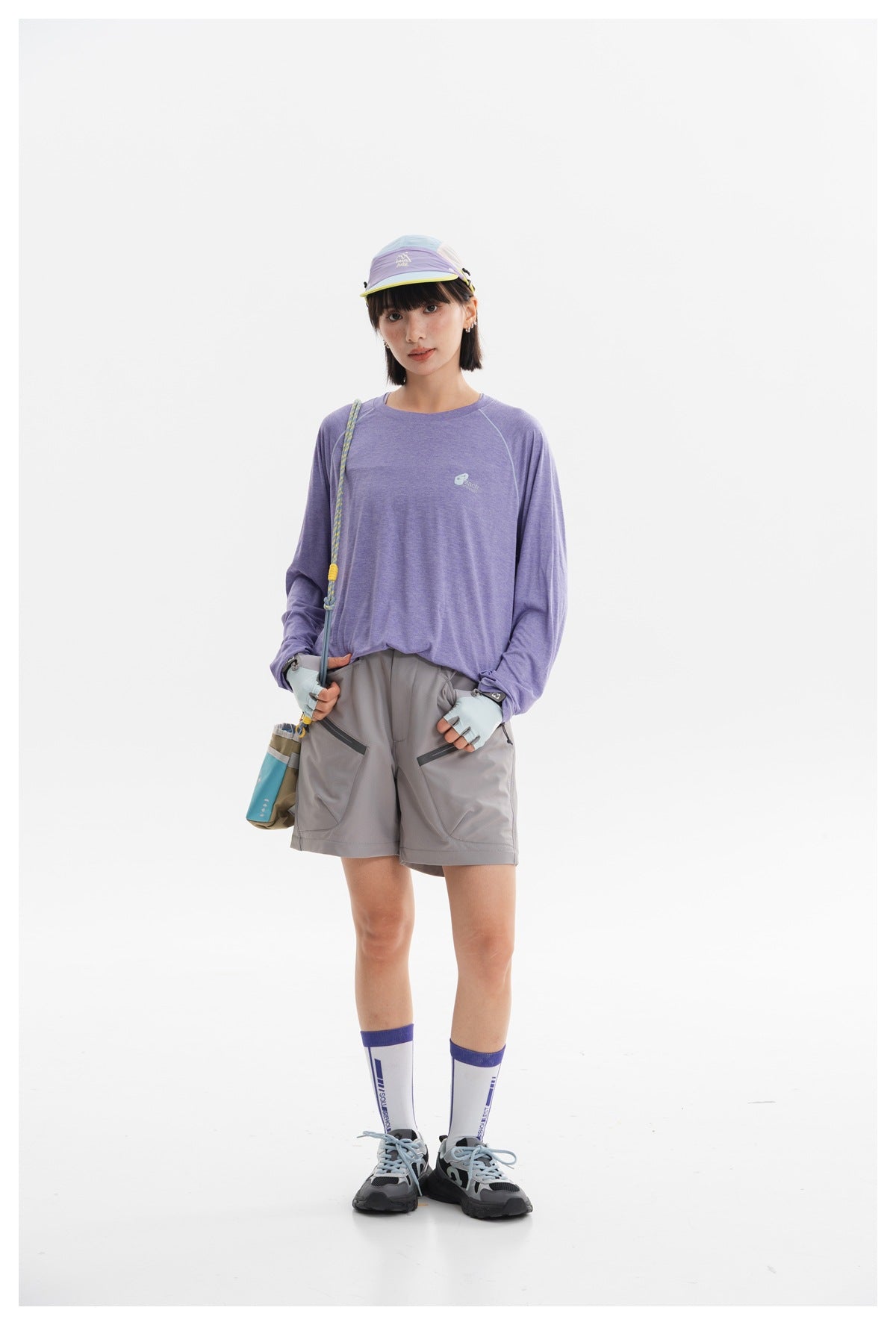 Model wearing a lavender long-sleeve top, gray shorts, a colorful visor, gloves, and hiking shoes.