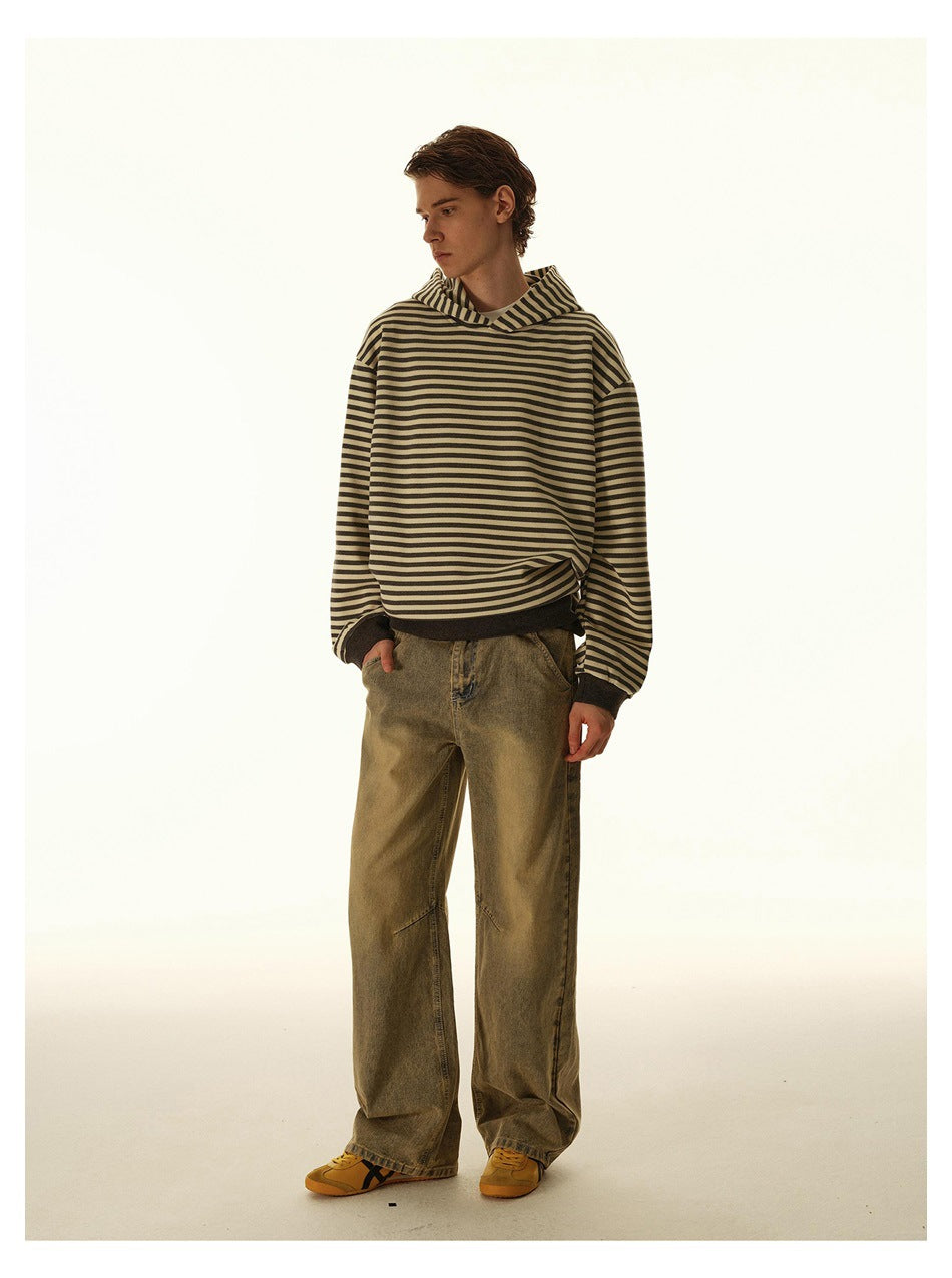 Model wearing a tan and dark striped hooded sweatshirt with dark cuffs and hem, paired with loose olive trousers.