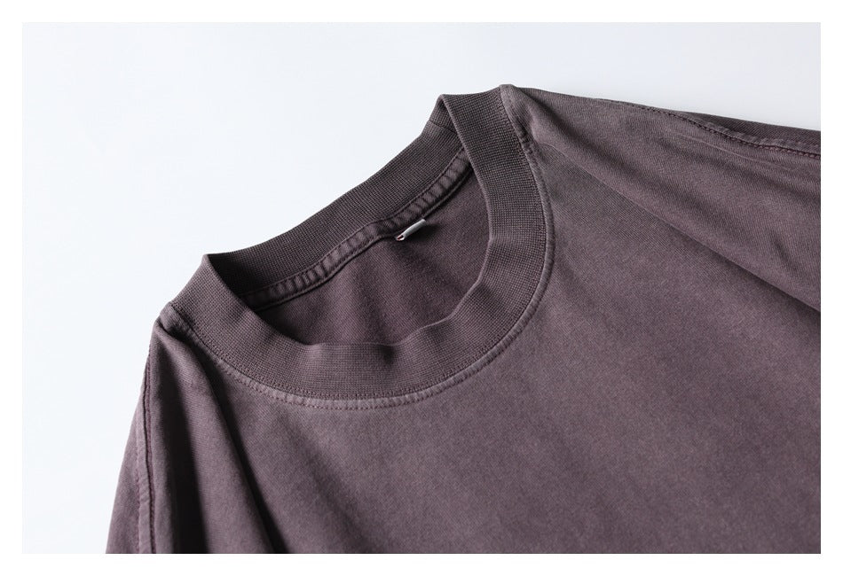 Close-up of the ribbed crew neckline, shoulder seam, and fabric of a muted plum T-shirt.
