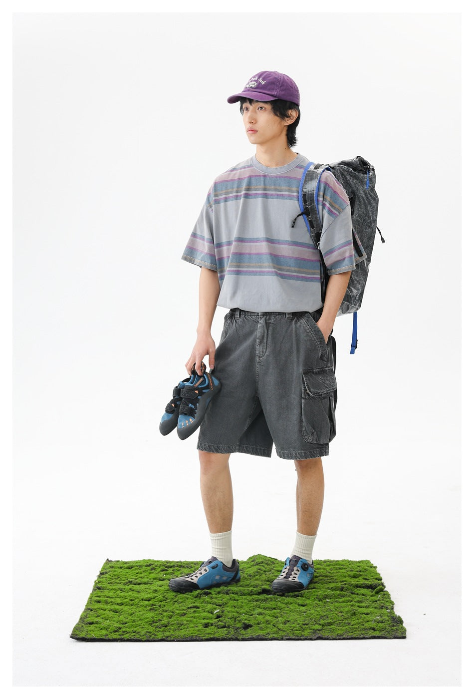 Three-quarter view of a model in a gray T-shirt with muted multicolor stripes and charcoal cargo shorts.