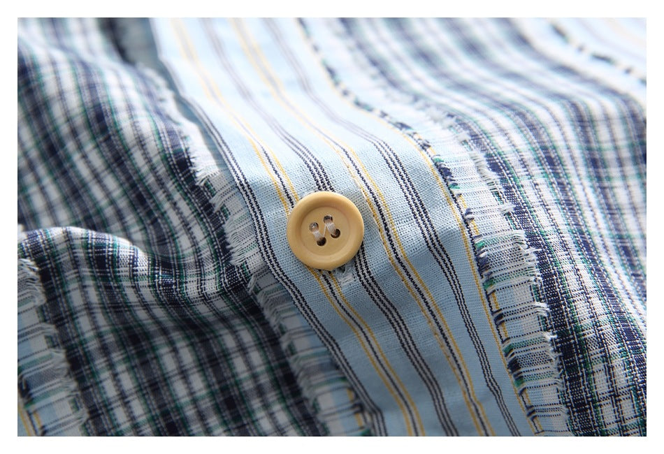 Close-up of a tan button on a light blue shirt placket with dark plaid and striped fabric panels.