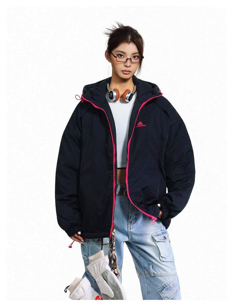 Model wearing a black hooded zip jacket with pink zipper over a white top and light-wash cargo jeans, holding gloves