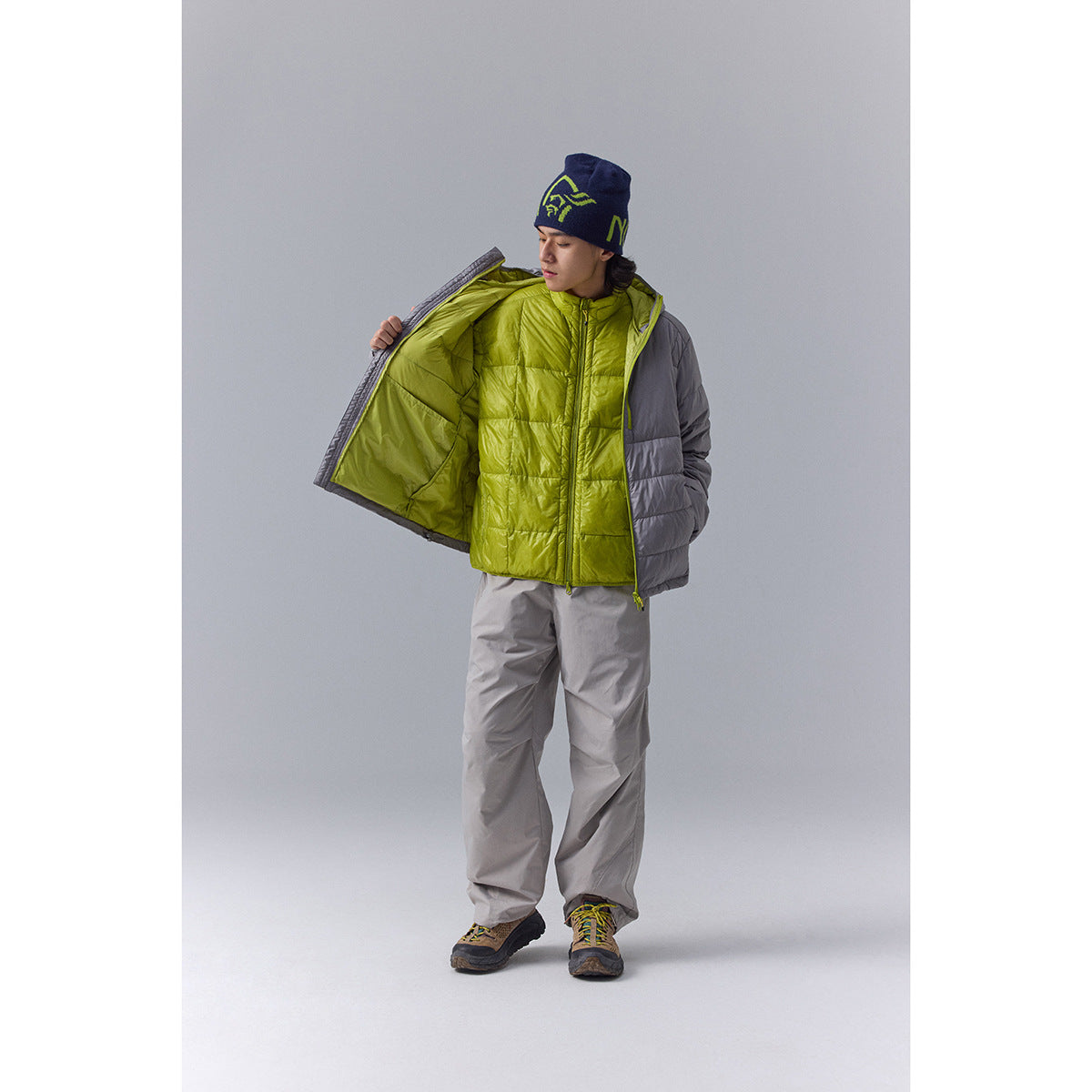 Model wearing a gray quilted puffer jacket open to show its bright lime lining, with gray outdoor trousers.