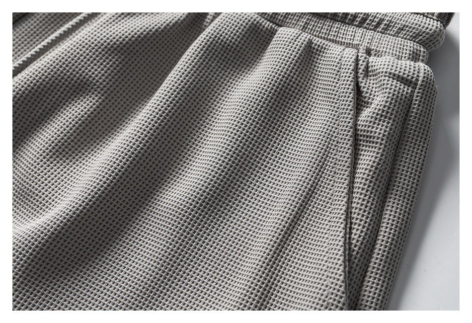 Close-up of light gray textured trousers showing a side pocket opening and stitching.