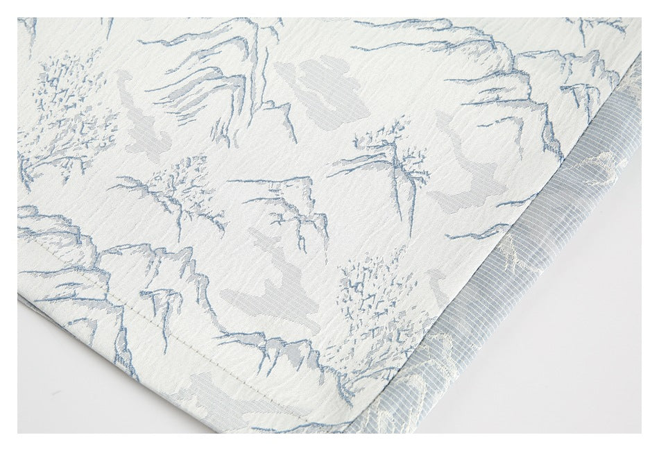 Close-up of off-white fabric with a pale blue mountain landscape print and a fine woven texture.