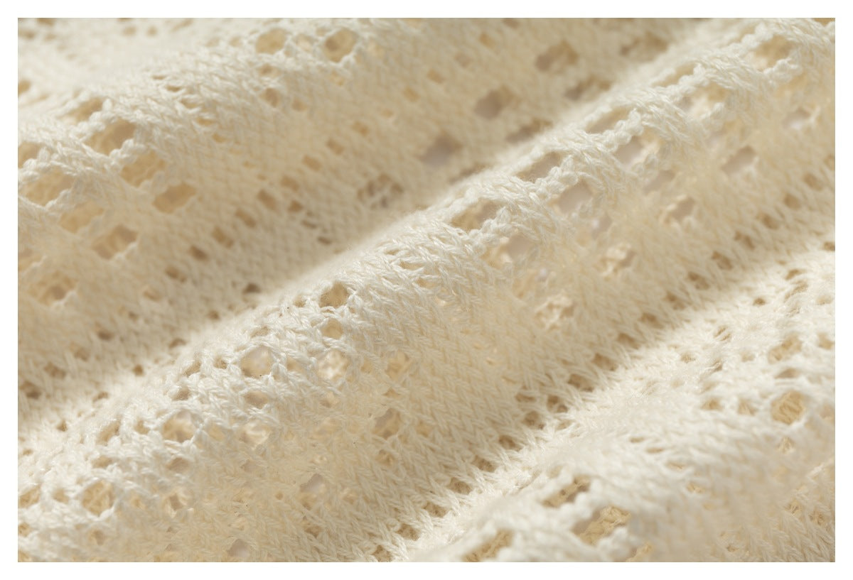 Macro view of the ivory garment's textured open-knit stitches and raised patterned bands.
