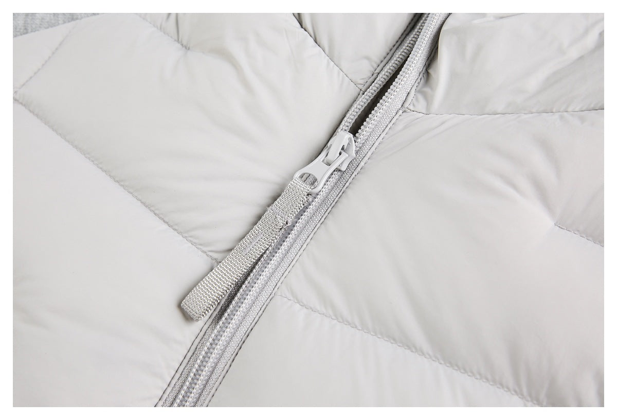 Close-up of a light gray jacket's front zipper, pull tab, and quilted panels.