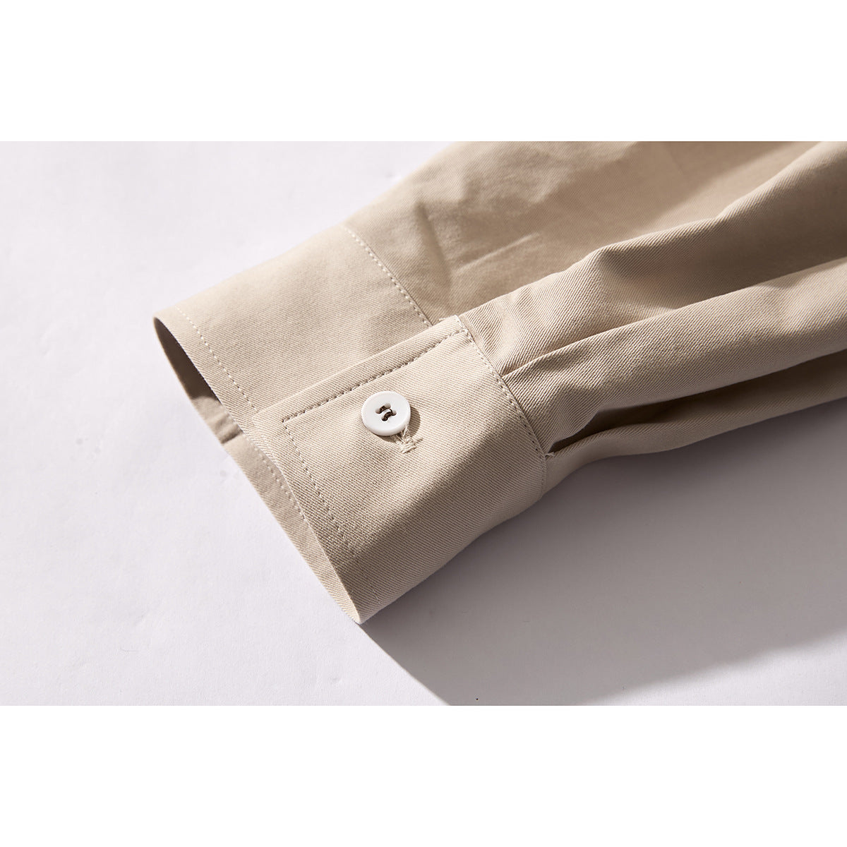 Close-up of a beige shirt cuff with a white button and visible stitching.