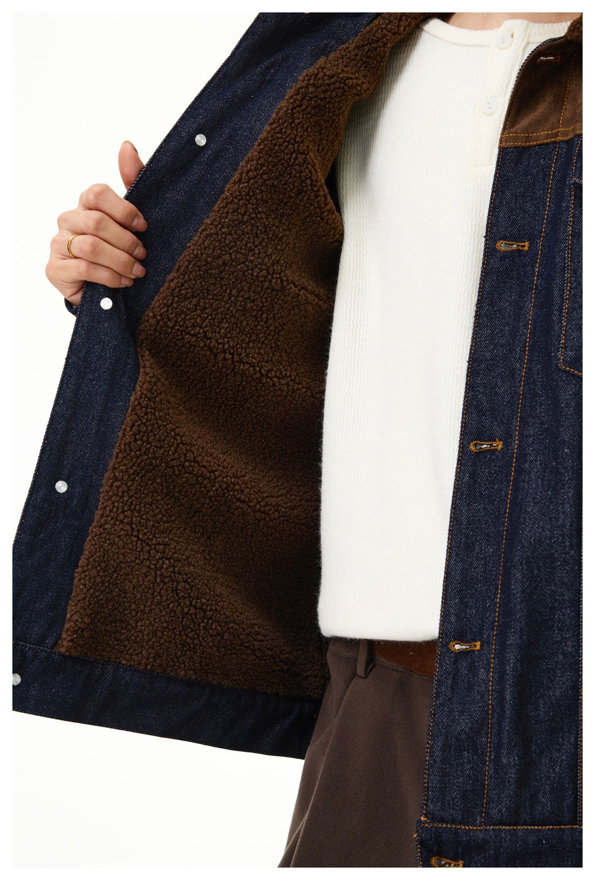 Close-up of a person wearing a dark indigo denim jacket with brown fleece lining, open over a white knit top.