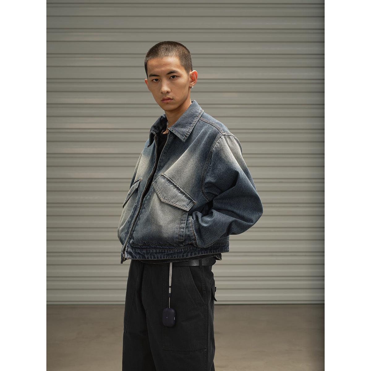 Front three-quarter view of a model in a faded blue denim jacket with flap pockets and black trousers.