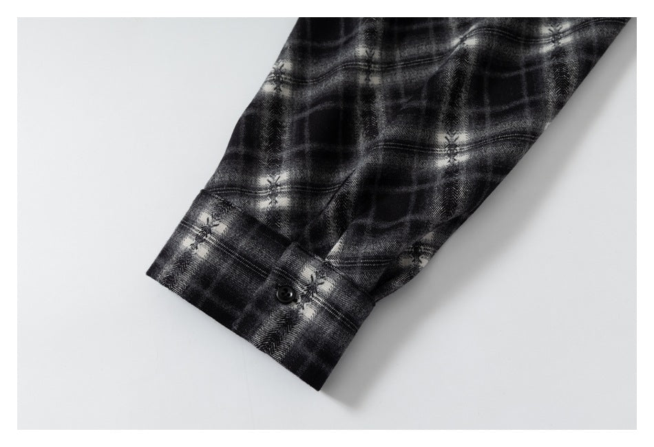 Close-up of a black and gray plaid shirt sleeve ending in a buttoned cuff.