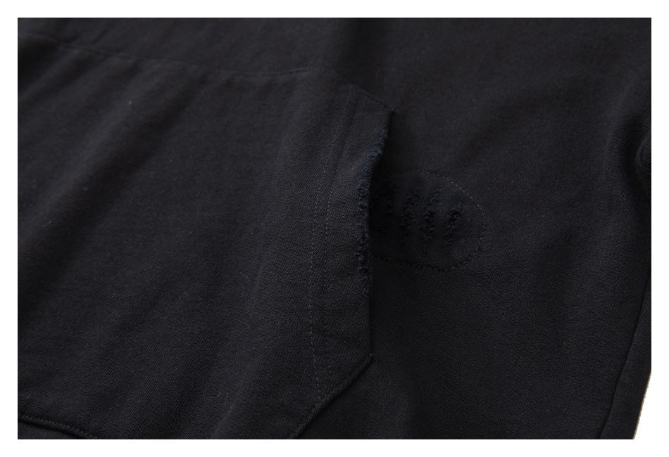 Close-up of a black hoodie pocket corner with a small distressed patch beside it.