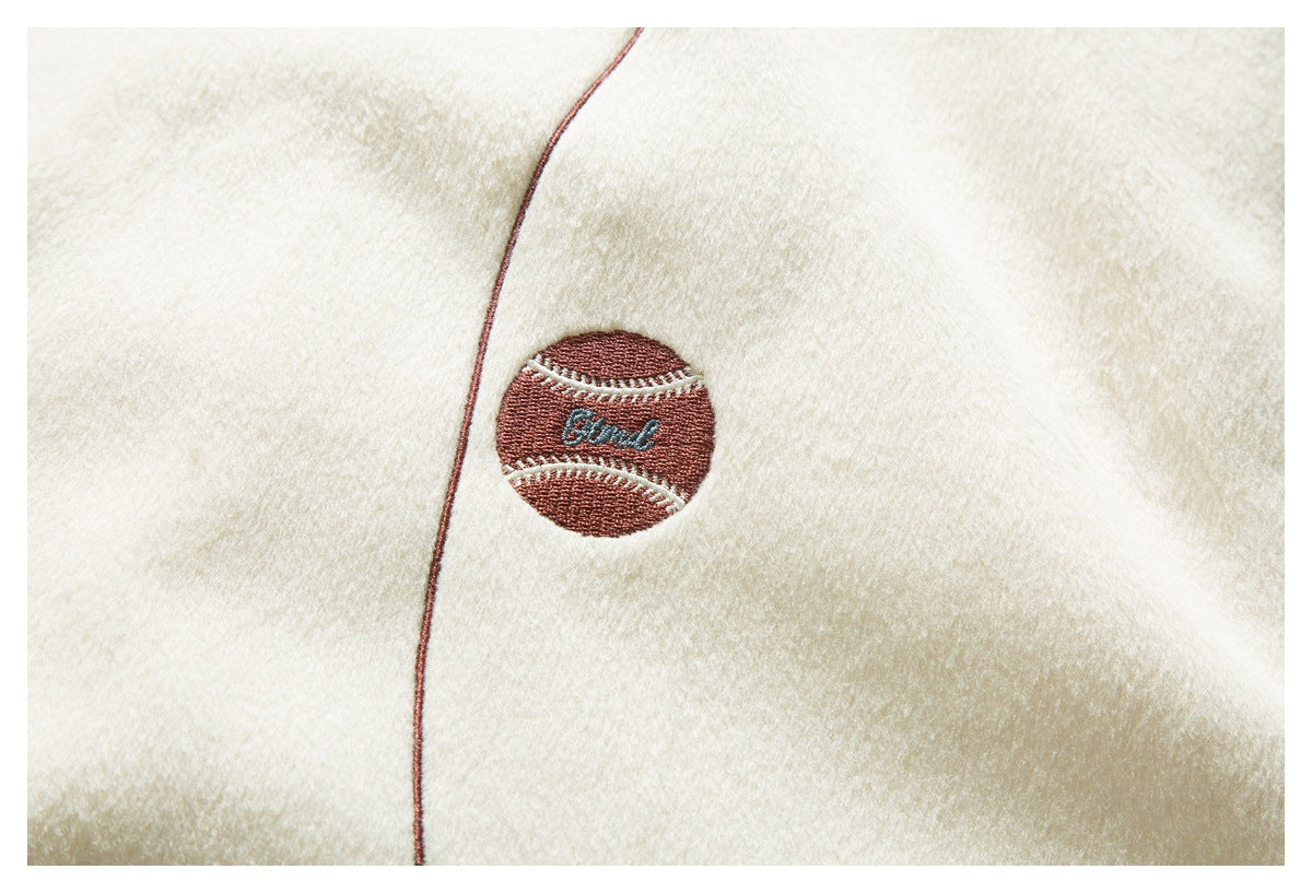 Close-up of a small embroidered baseball-shaped patch on cream fabric beside a contrasting seam.