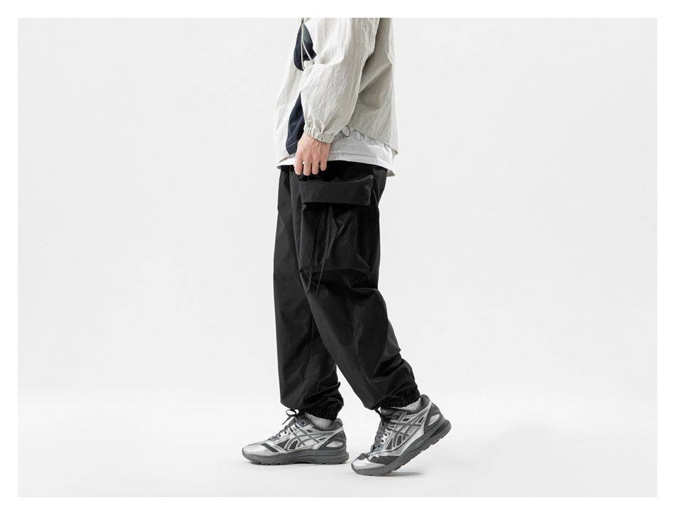 Side view of a model wearing black cargo jogger pants with a large flap pocket and elastic cuffs.