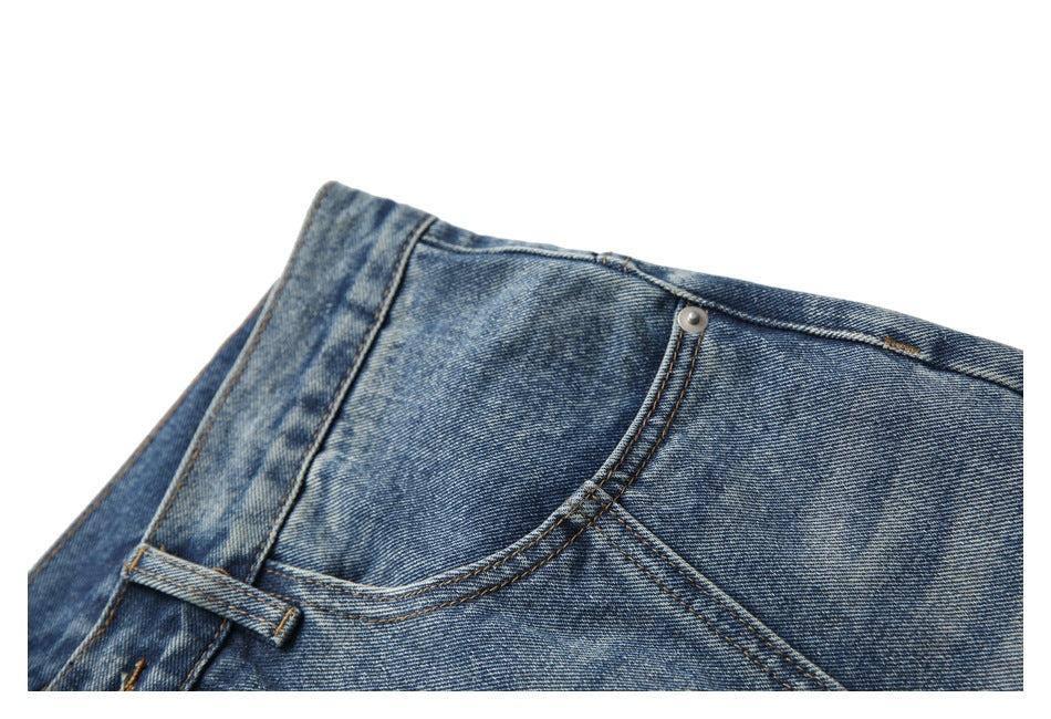 Close-up of blue washed jeans showing the curved front pocket, waistband, belt loop, and metal rivet.