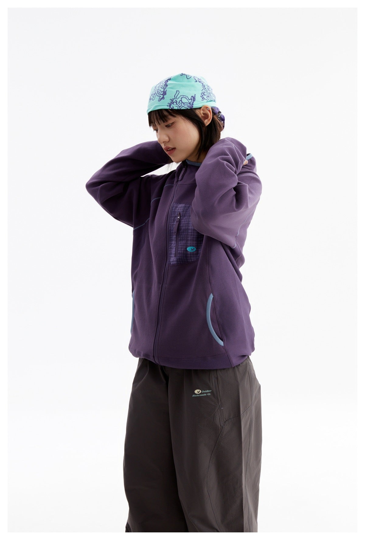 Side-angle view of a woman wearing a purple hooded jacket with a checked chest pocket and dark pants.