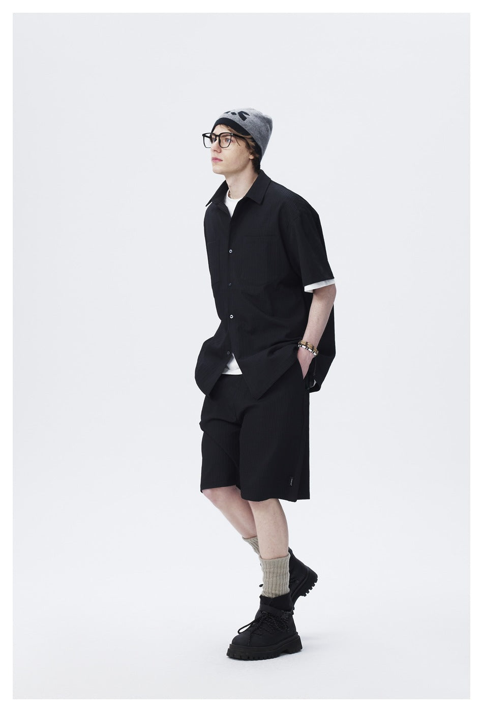 Three-quarter view of a model wearing a black short-sleeve button-up shirt and matching shorts.
