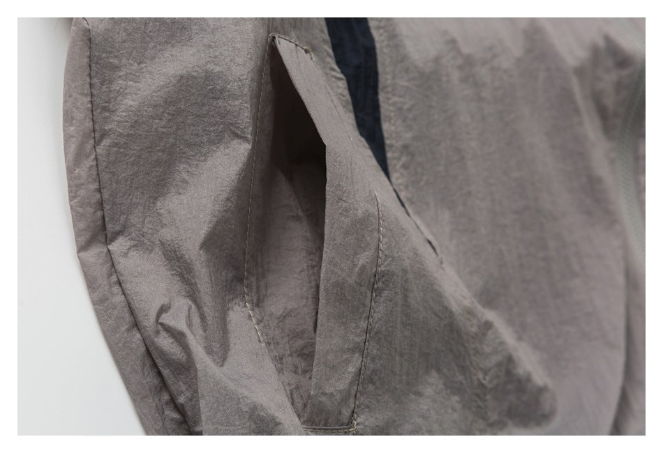 Close-up of an angled pocket opening on a taupe-gray crinkled garment with a dark contrast panel.