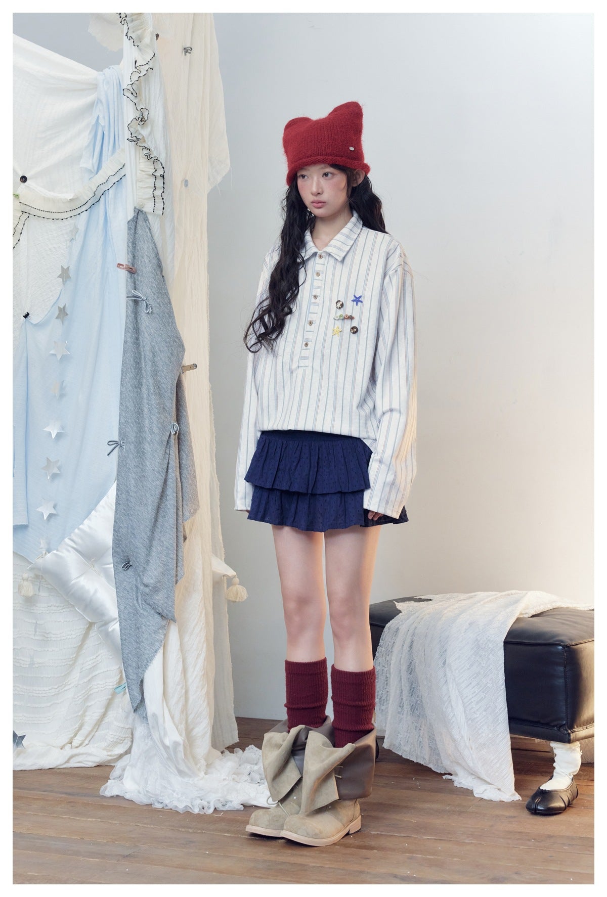 Full-length model wearing a white striped long-sleeve shirt with decorative charms and a navy tiered skirt.